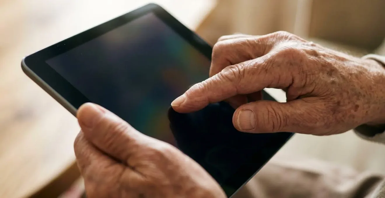 Gros plan macro sur des mains âgées interagissant avec une tablette dans une lumière douce, évoquant l'adaptation technologique